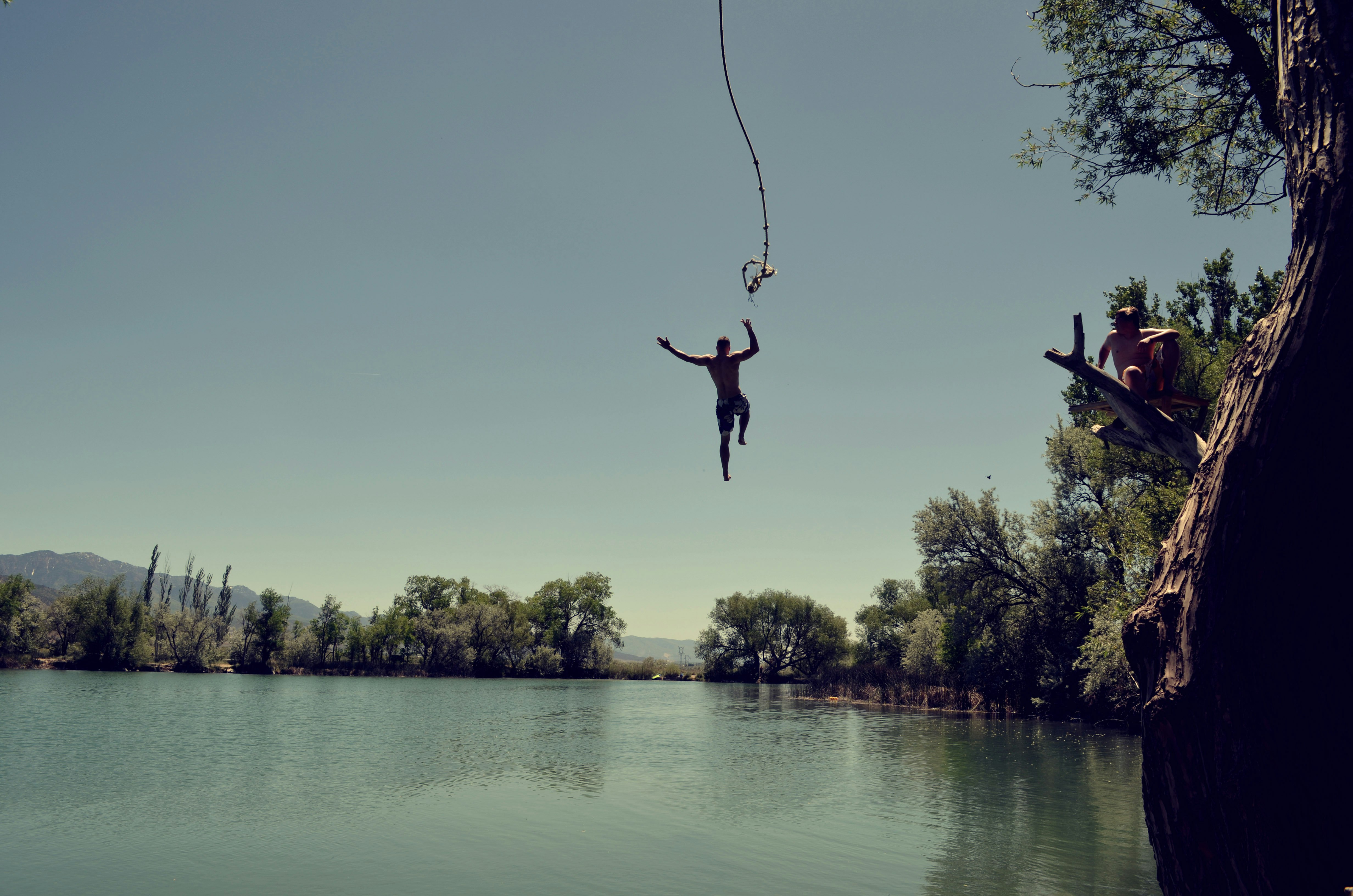 man jumping on body of water with rope